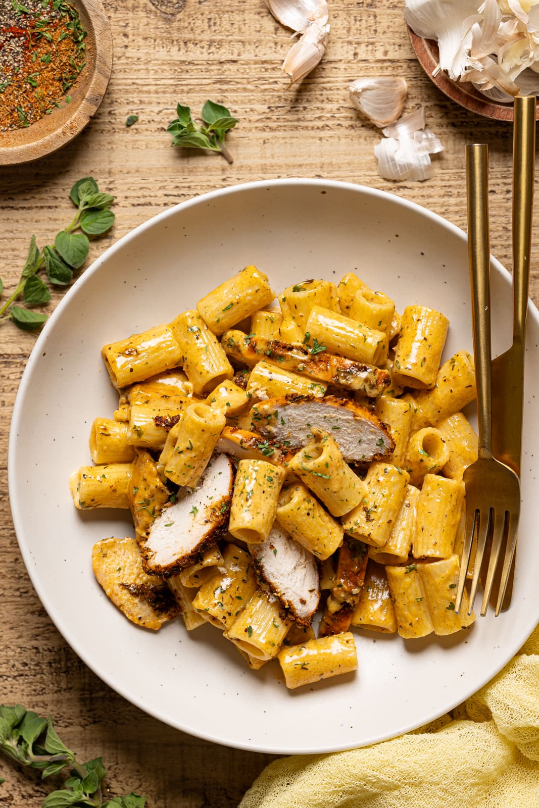 Chicken pasta with a white plate with a knife and fork with garlic and herbs as garnish.