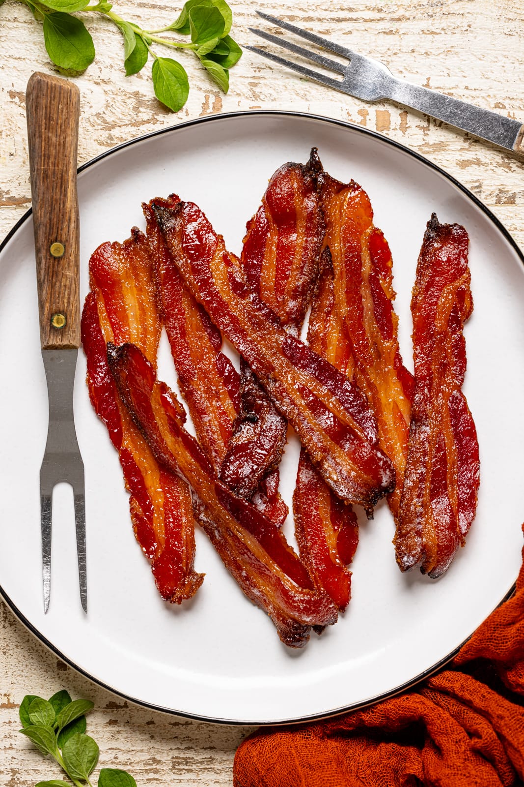 Cooked bacon on a white plate with two forks.