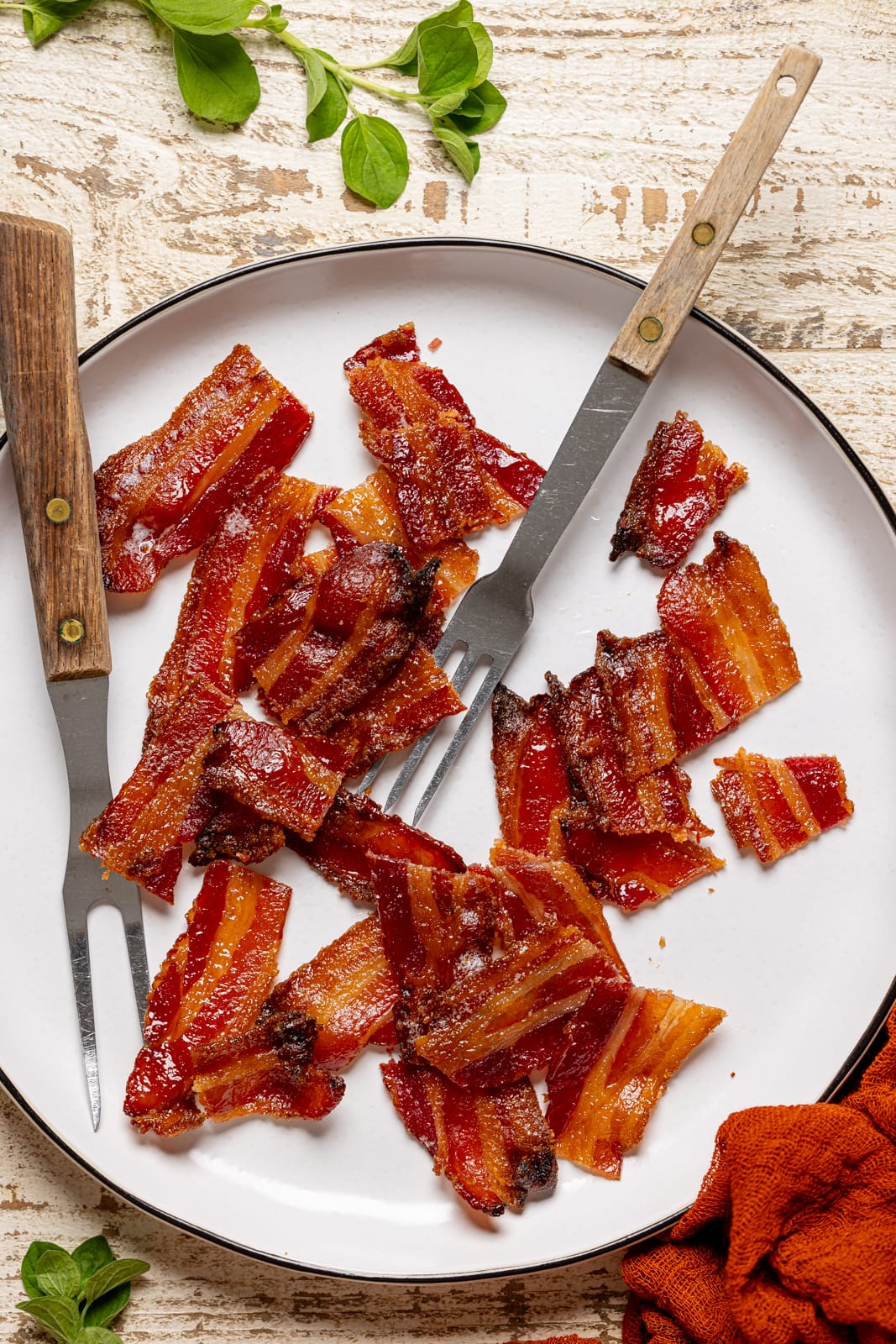 Bacon chopped into medium chunks on a white plate with two forks. Candied bacon recipe