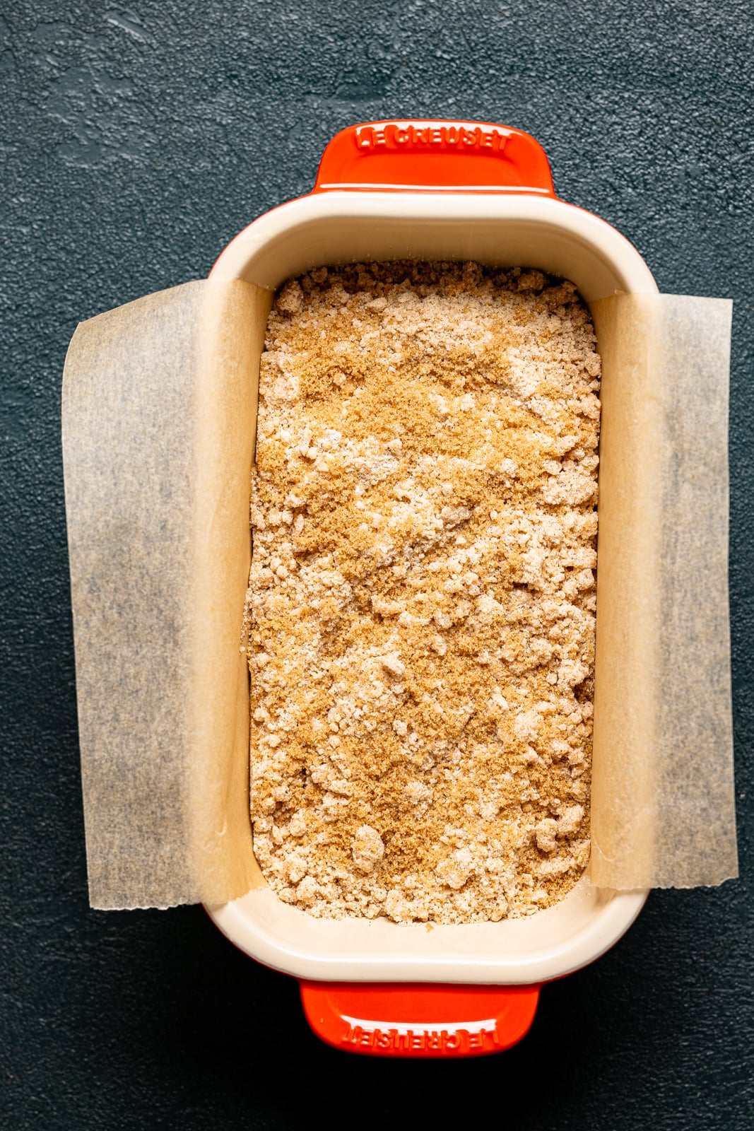 Bread batter in a red bread pan with toppings and parchment paper.