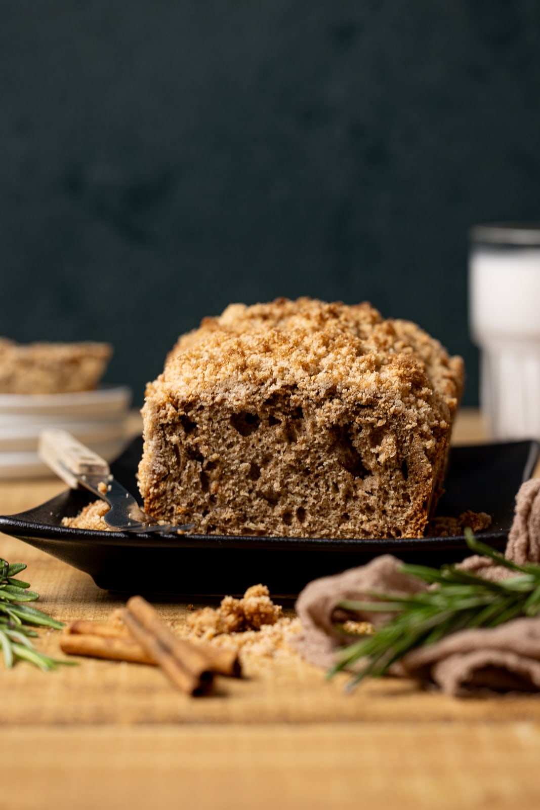 Cinnamon quick bread sliced on a black platter with a glass of milk, and stacks of plates in the background. 