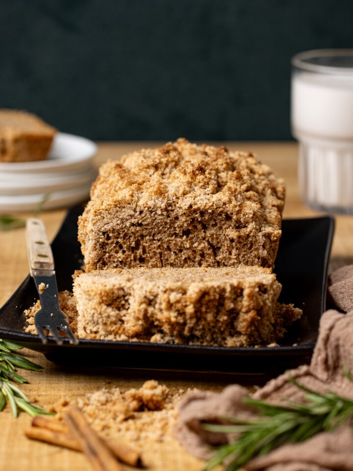 Bread sliced on a black platter with cinnamons ticks, rosemary, and glass of milk.