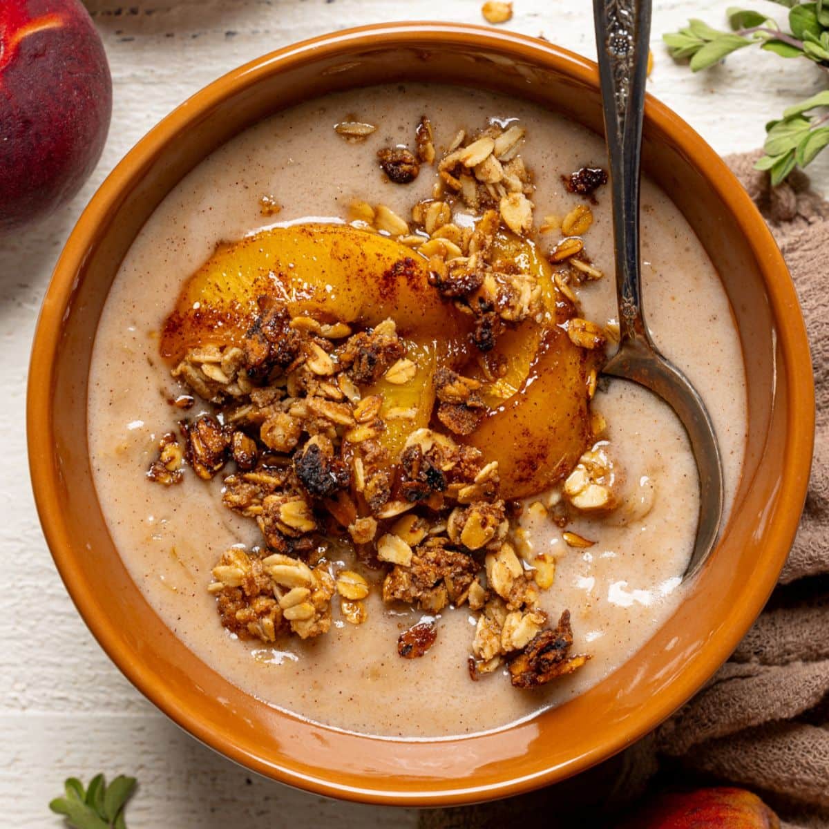 Up close shot of porridge in a bowl with a spoon, peaches, and granola.