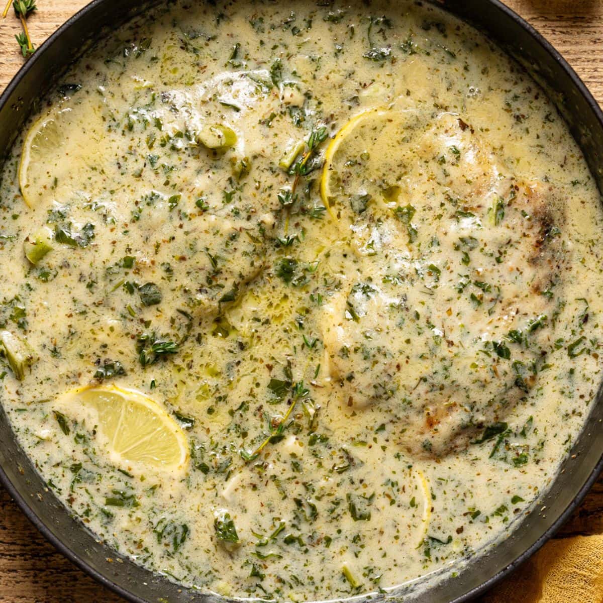 Creamy tilapia in black skillet with thyme sprigs and lemon.