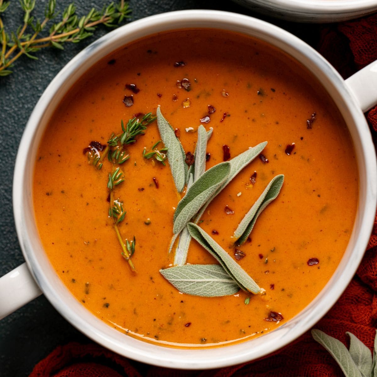 Soup in two white bowls with a garnish of sage and thyme.