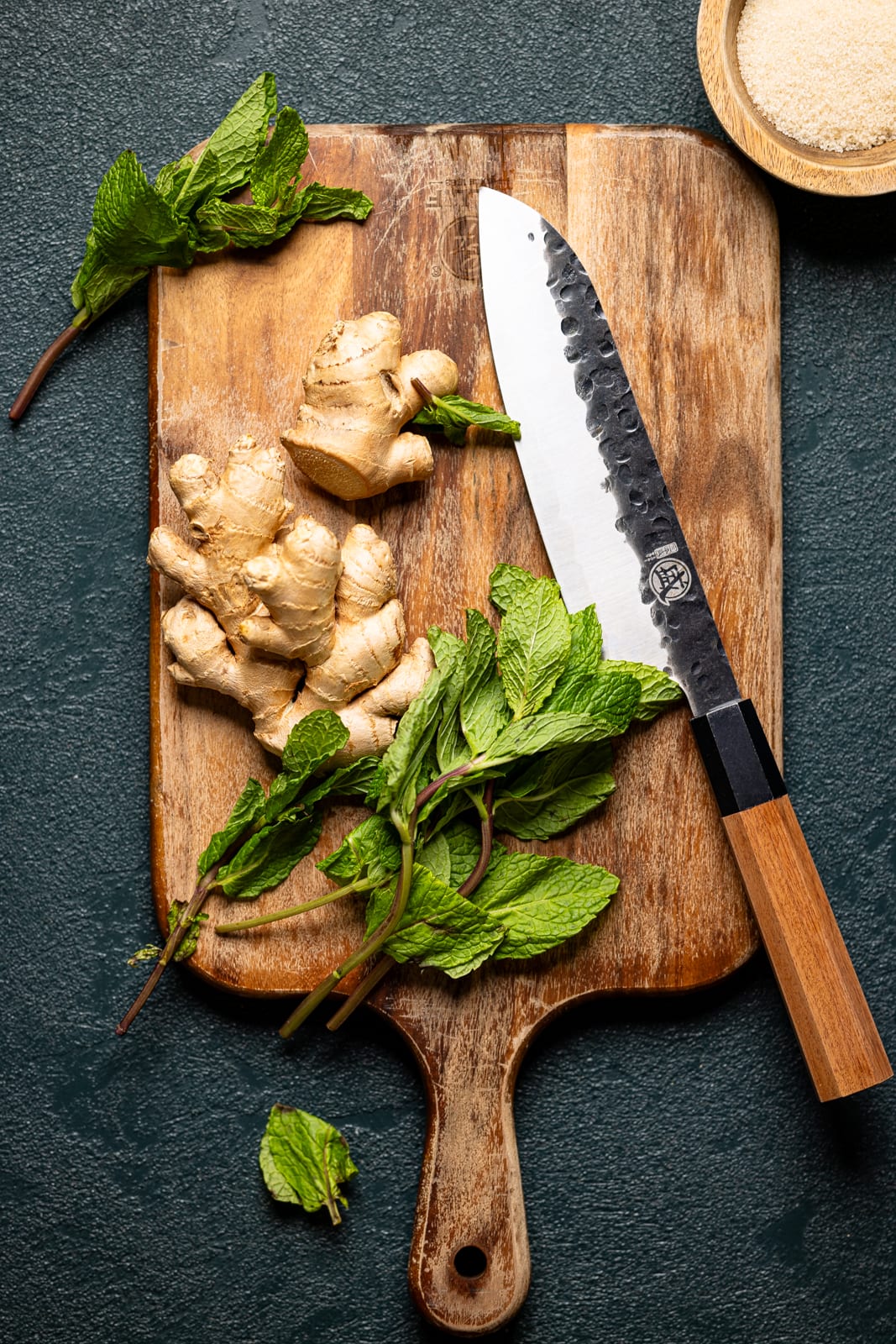 Ginger root and fresh mint leaves on a cutting board with a knife.