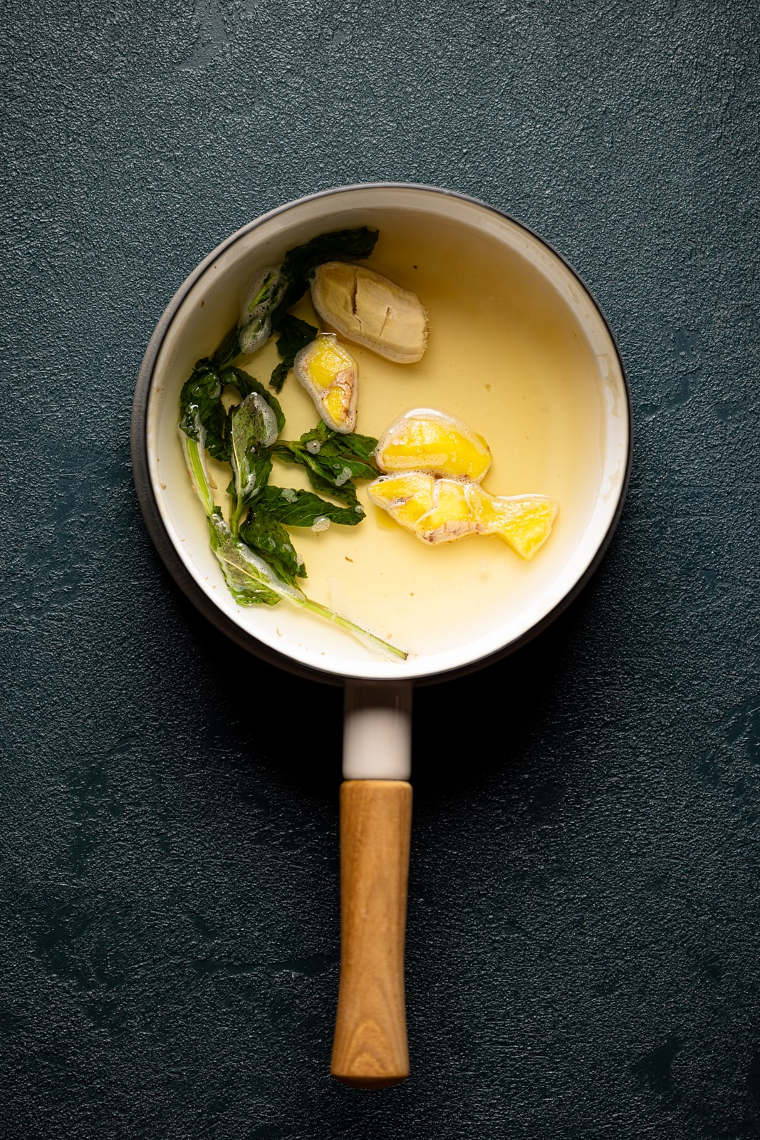 Ginger mint syrup in a saucepan on a dark green table for ginger mocktail recipe.