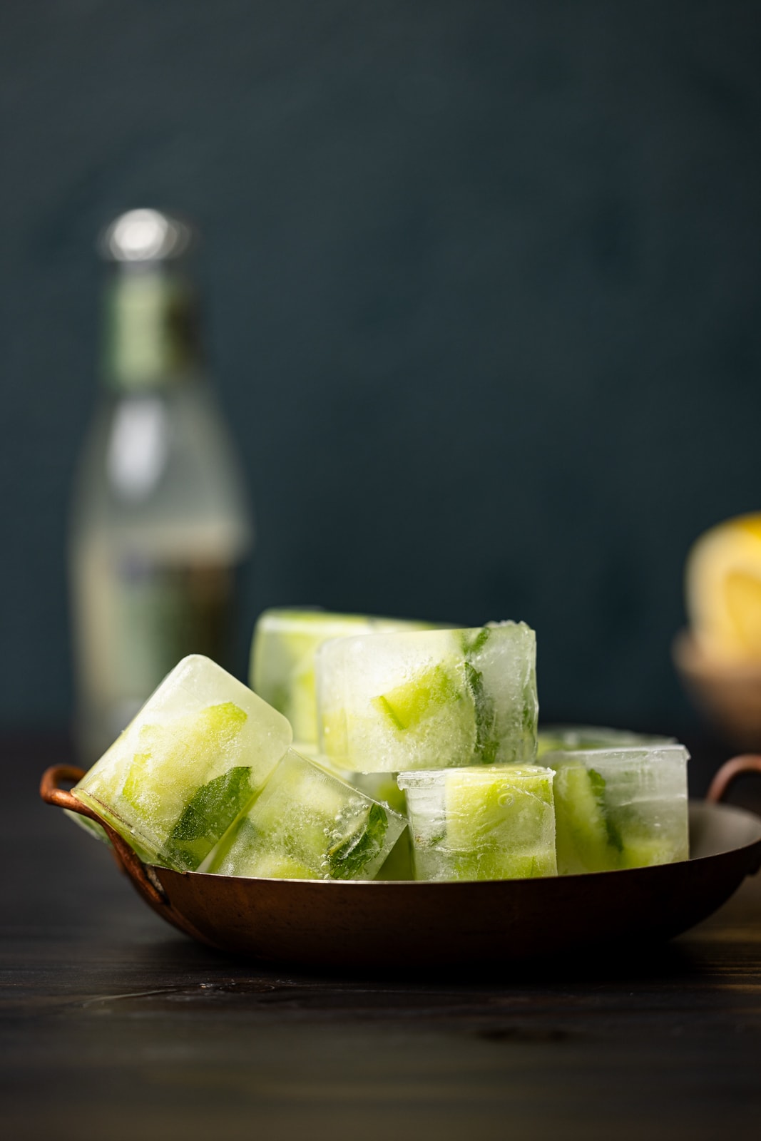 Ice cubes in a bowl on a black table with a bottle of ginger beer in background.