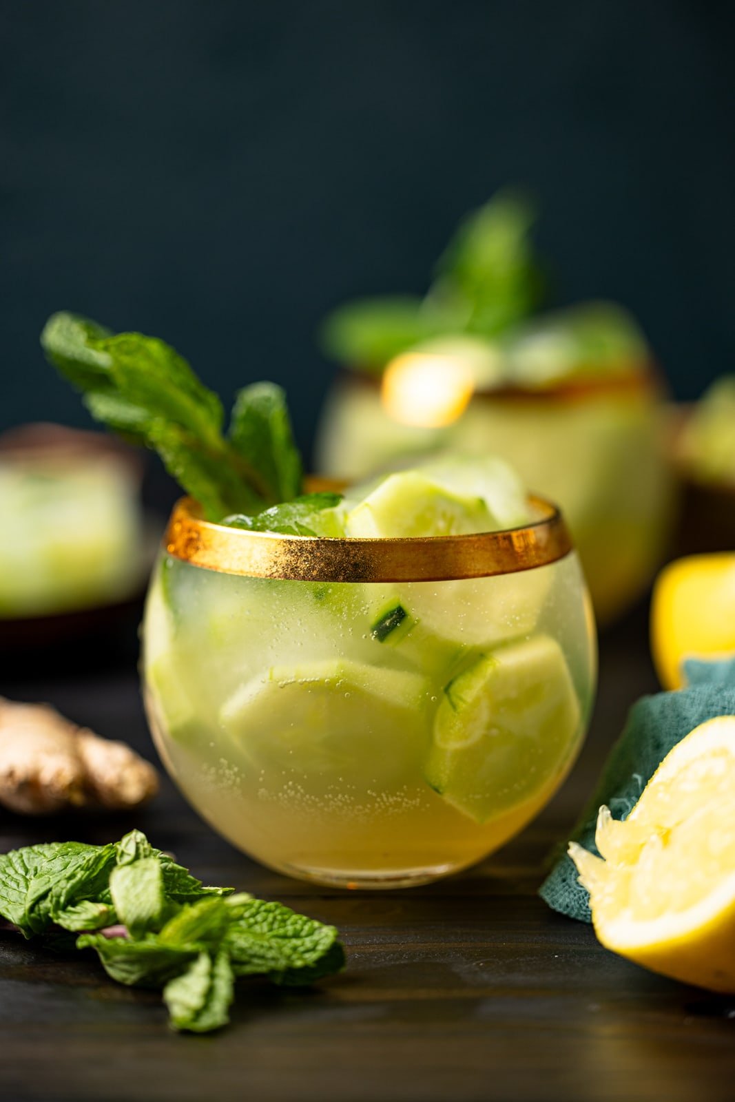 Two glasses of cucumber mint mocktail with lemons and herbs. 