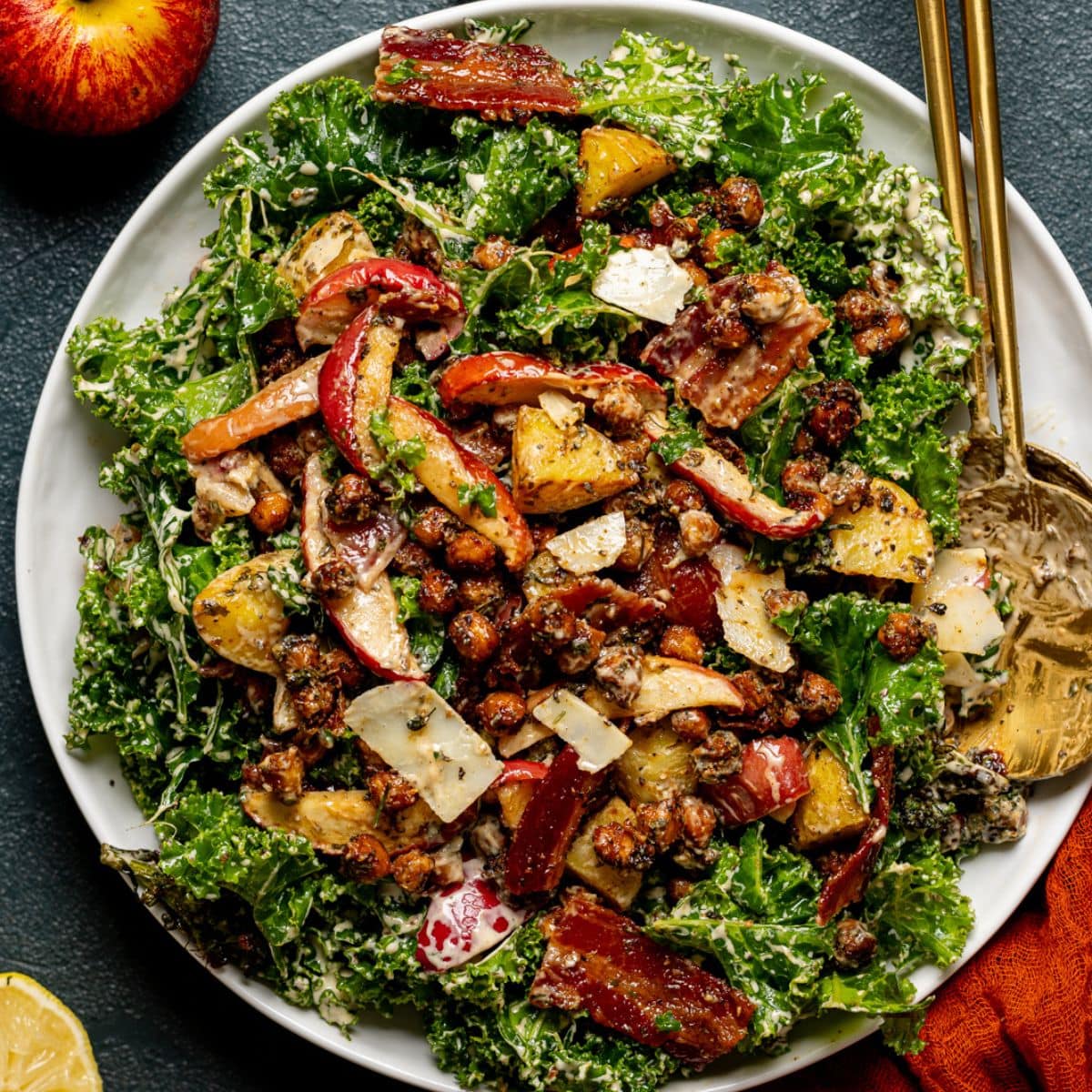 Full kale salad tossed in dressing with two gold serving spoons.