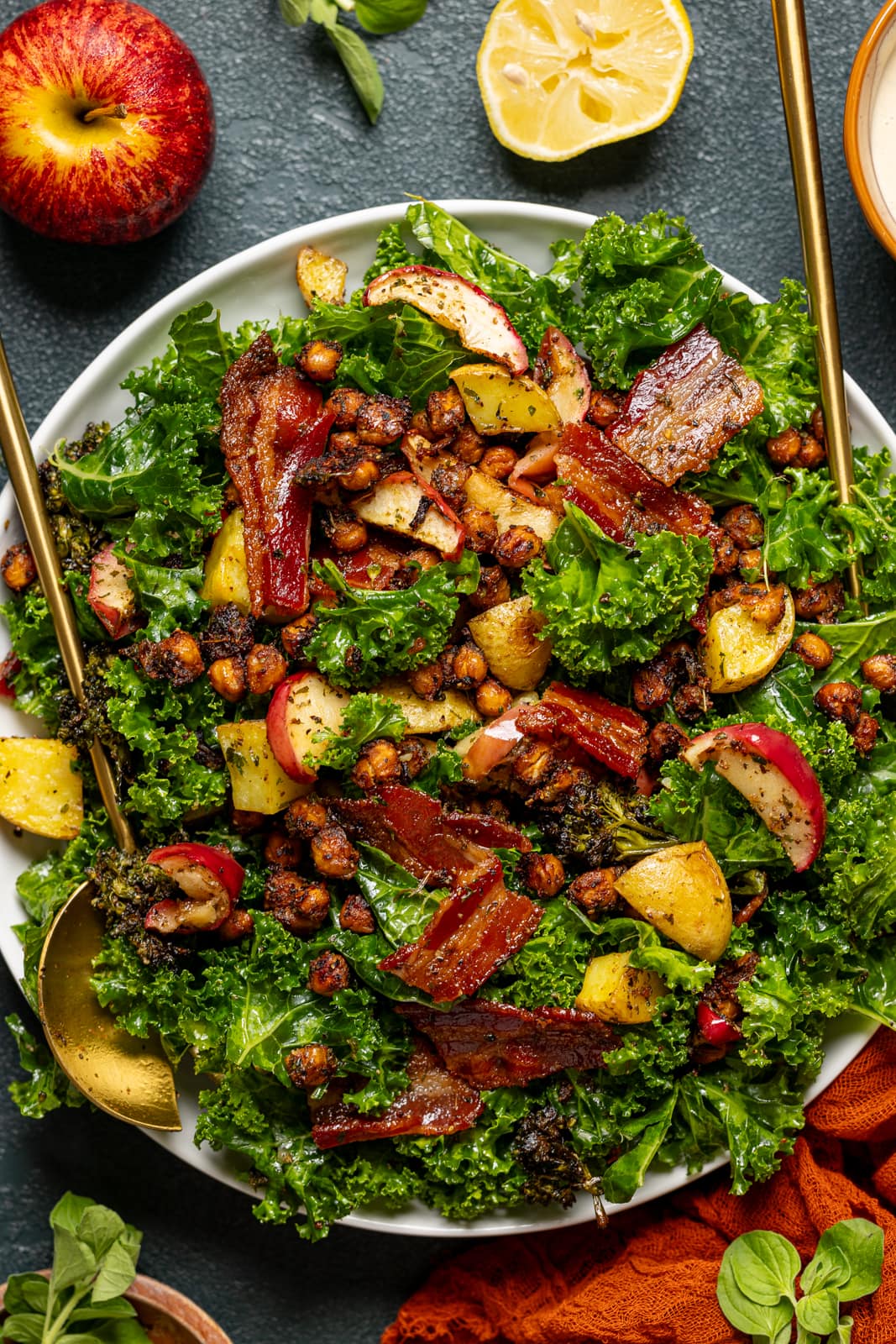 Full kale salad on a round serving dish with two gold serving spoons.