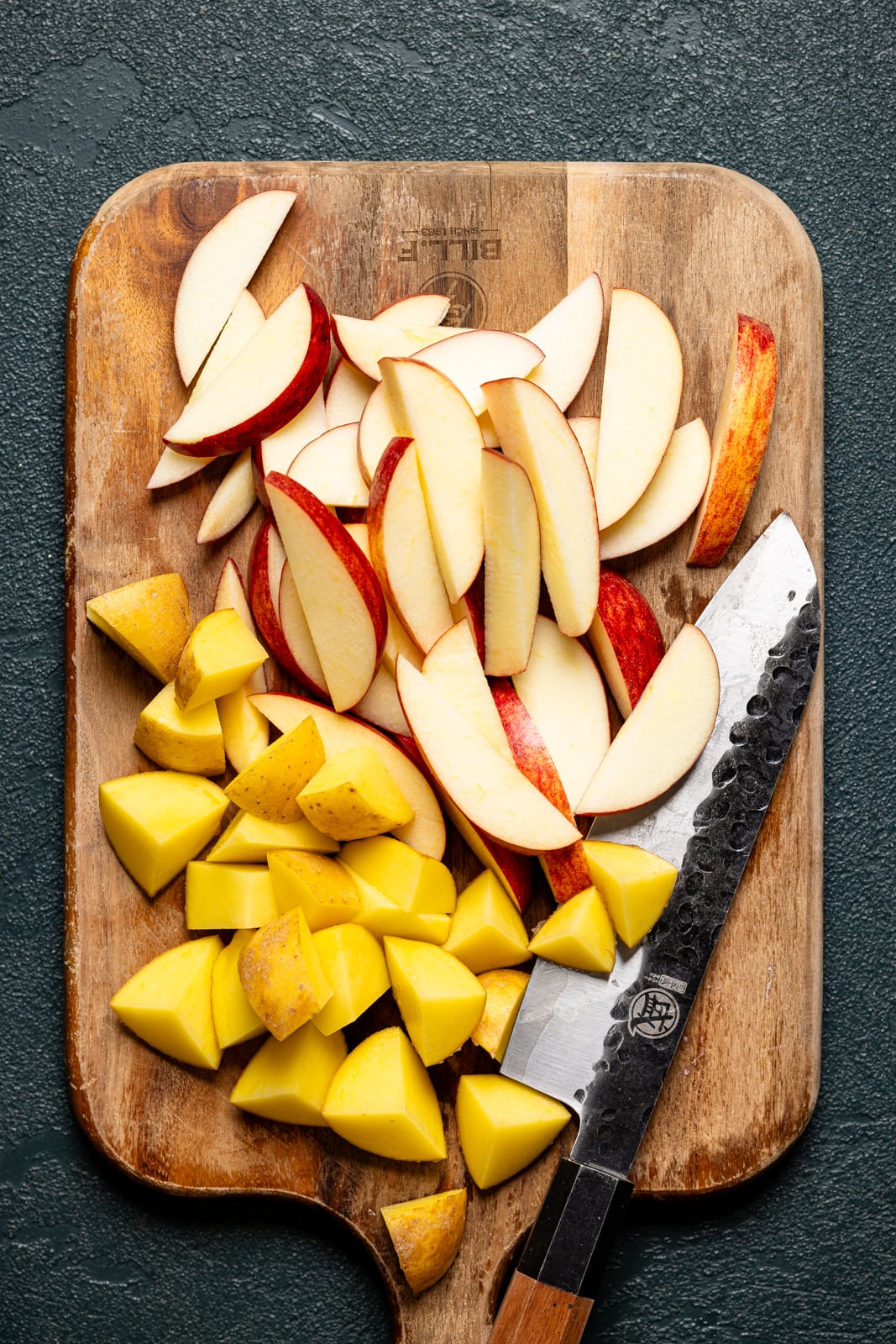 Chopped apples and potatoes on a cutting board with a knife.