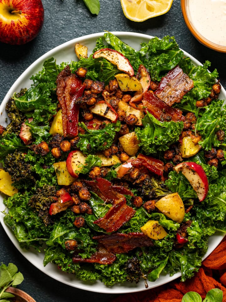 Full kale salad on a white serving dish with an apple, lemon, and red napkin.