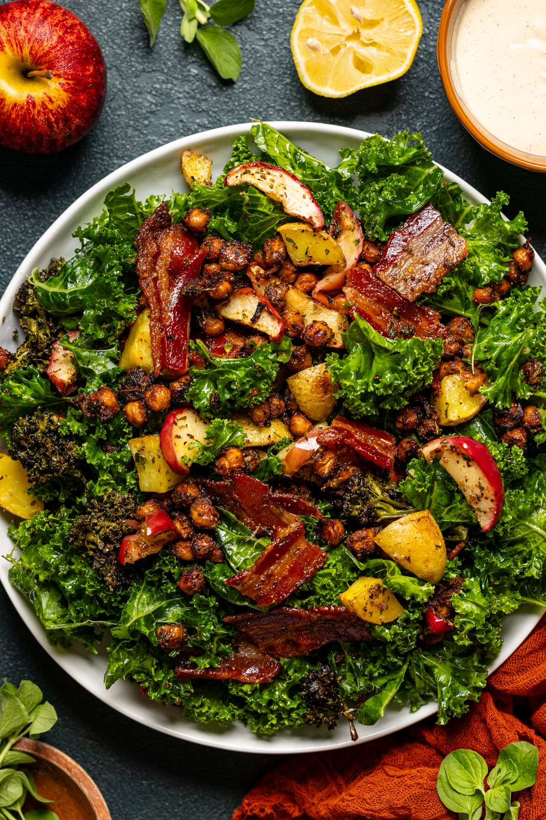 Full kale salad on a white serving dish with an apple, lemon, and red napkin.