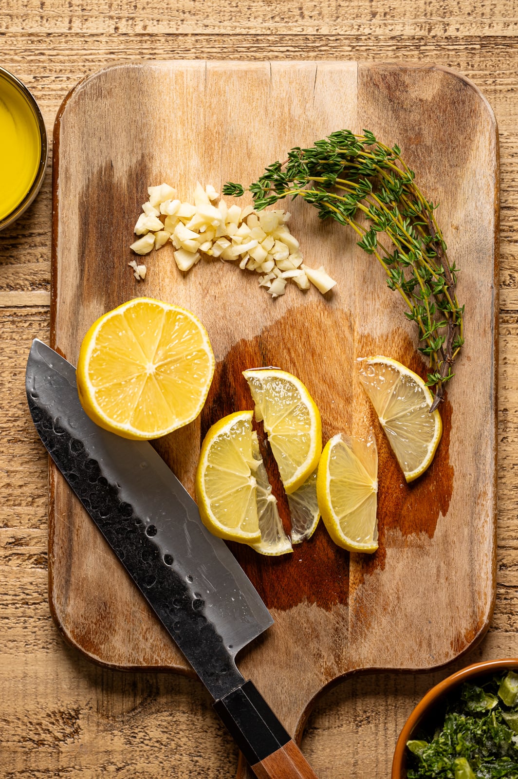 Chopped lemon, garlic, and thyme sprigs on a cutting board with a knife. 