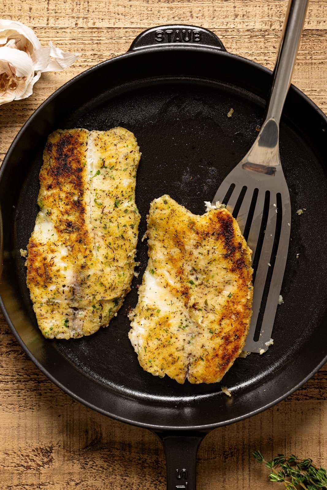 Seared tilapia in a black skillet with a spatula. 