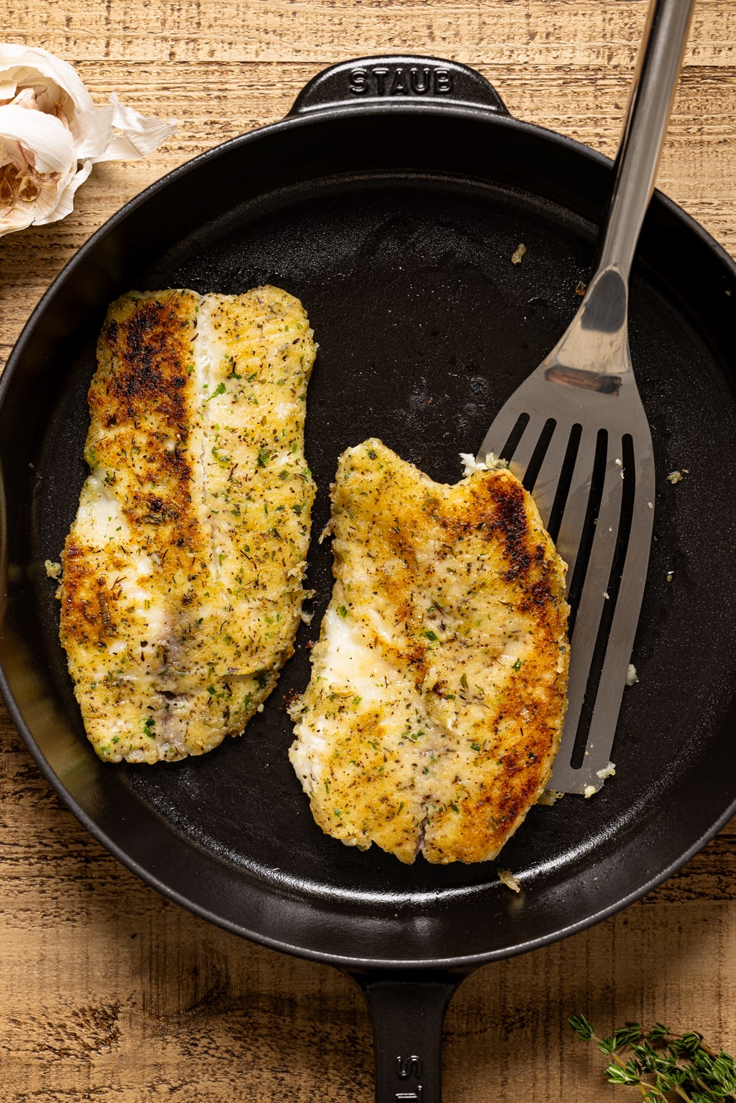 Seared tilapia in a black skillet with a spatula. 