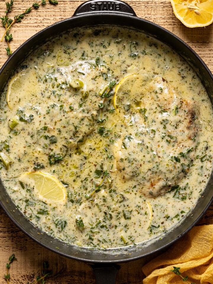 Creamy tilapia in black skillet with thyme sprigs and lemon.