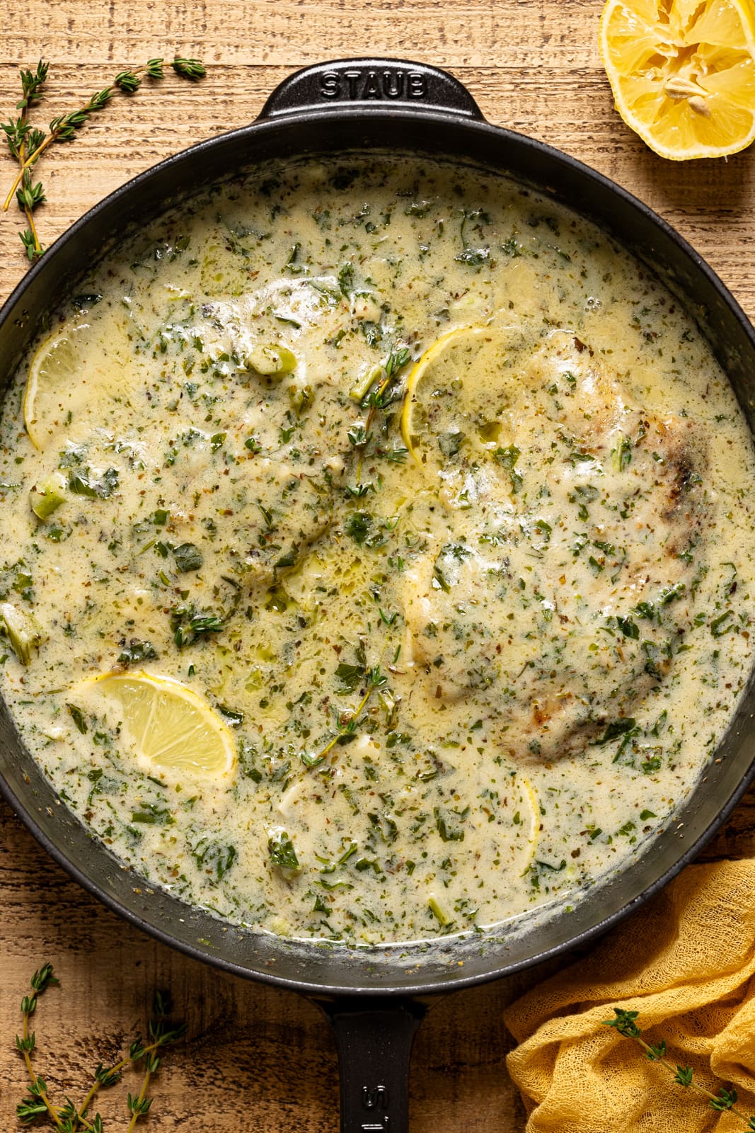 Creamy tilapia in black skillet with thyme sprigs and lemon.