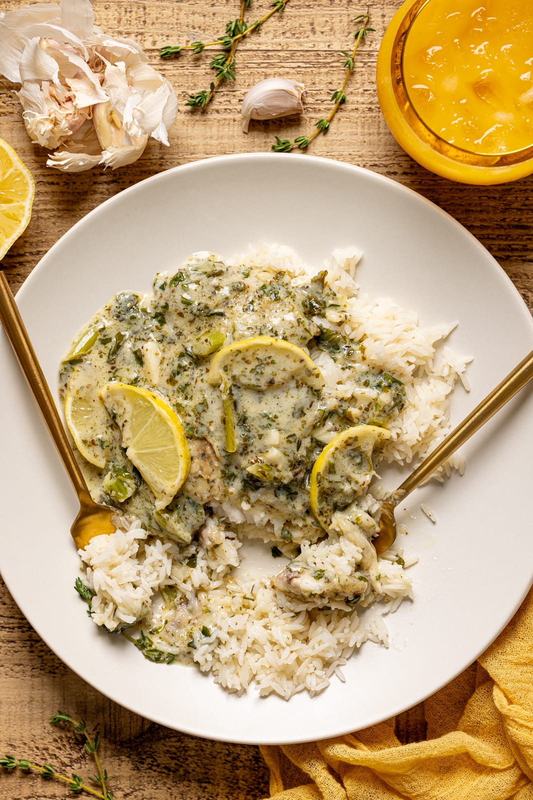 Creamy tilapia and rice with two forks, glass of juice, garlic, and lemon.