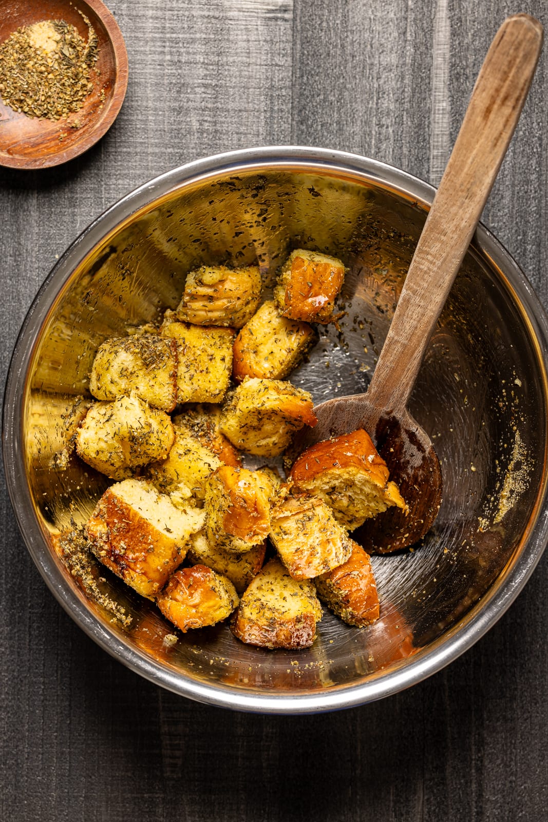 Bowl with garlic bread cubes with a wooden spoon and seasonings. 