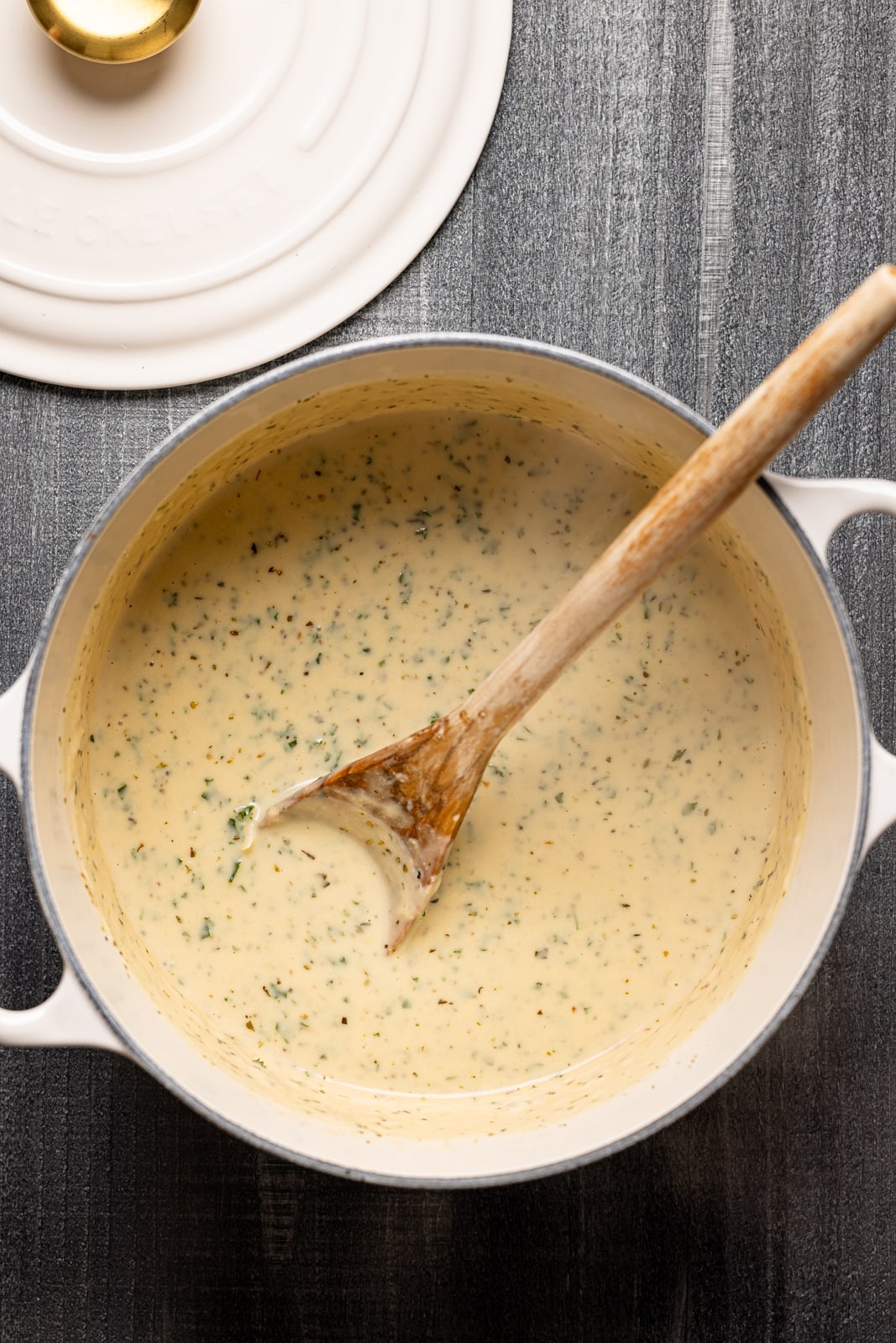 Soup in a white dutch pot with a wooden spoon.