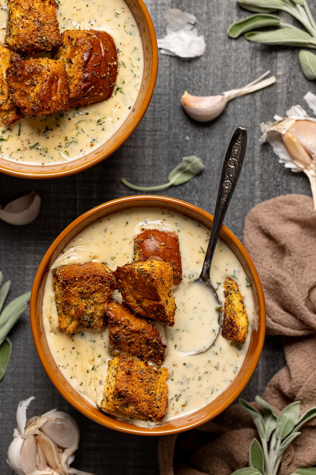 Two bowls of soup with garnish of garlic bread, garlic, and a spoon.