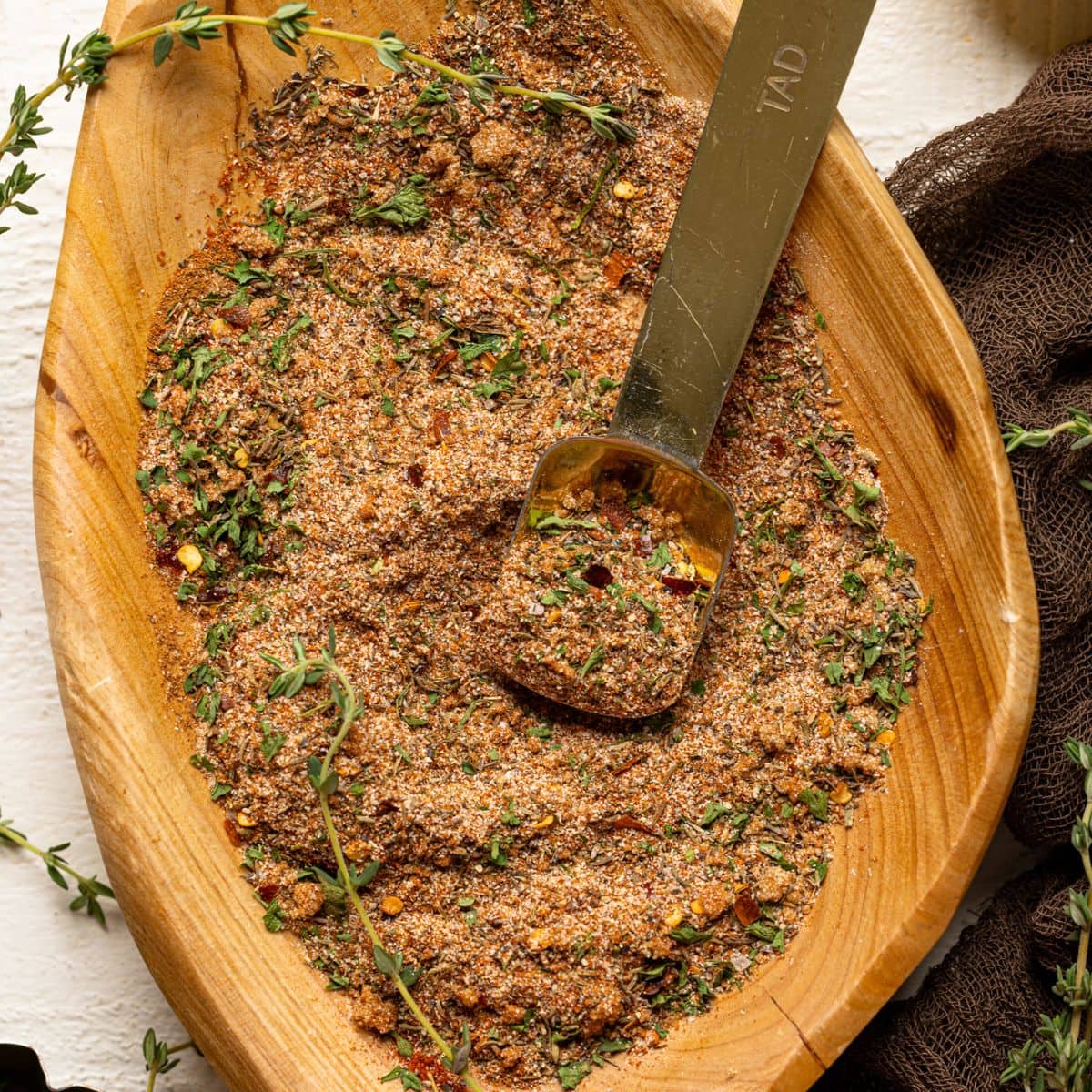 Seasoning blend in a wood bowl with thyme sprigs and gold spoon.