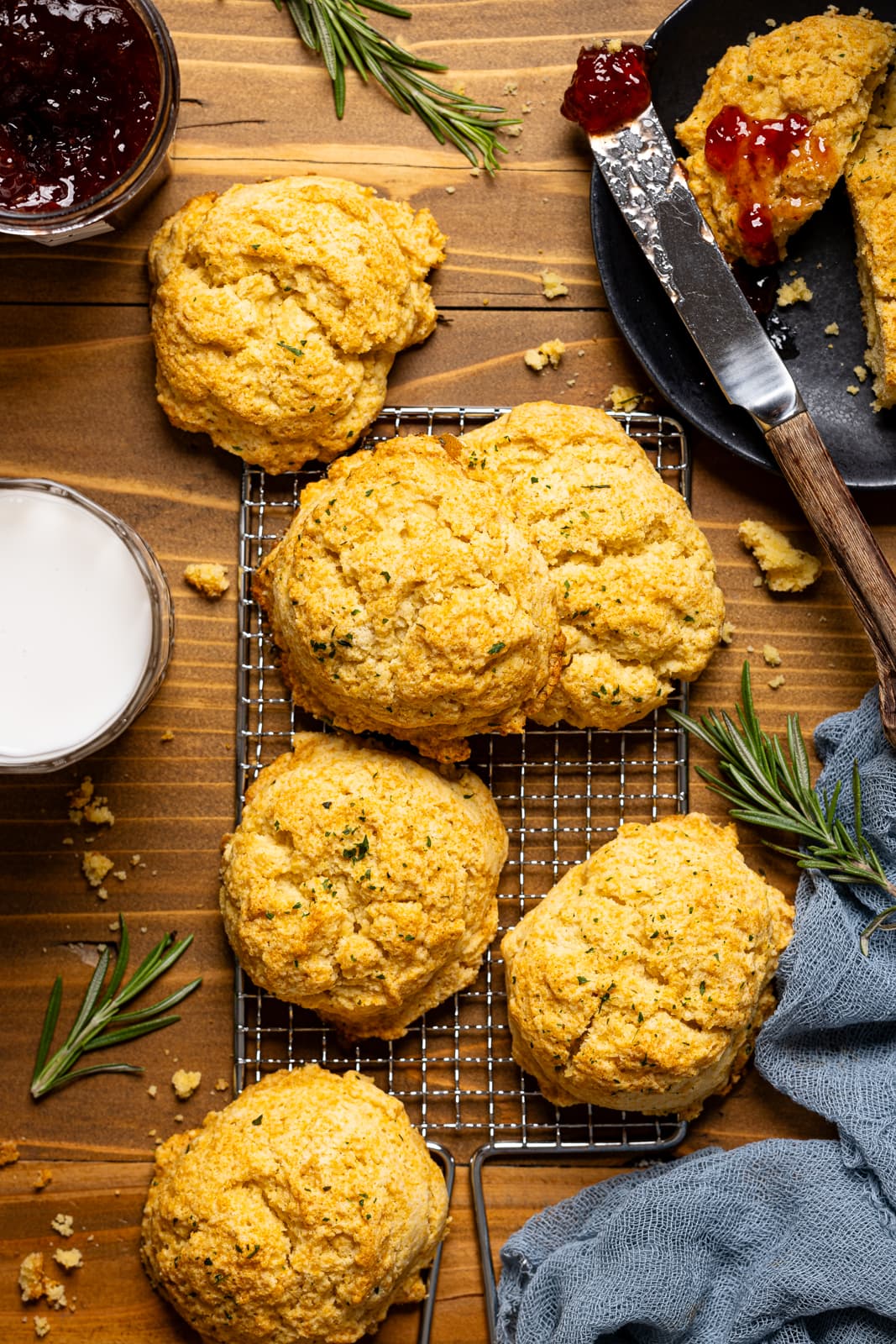 Biscuits on a brown wood table with a glass of milk, jam, and a plate with knife. 