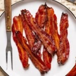 Cooked bacon on a white plate with two forks.