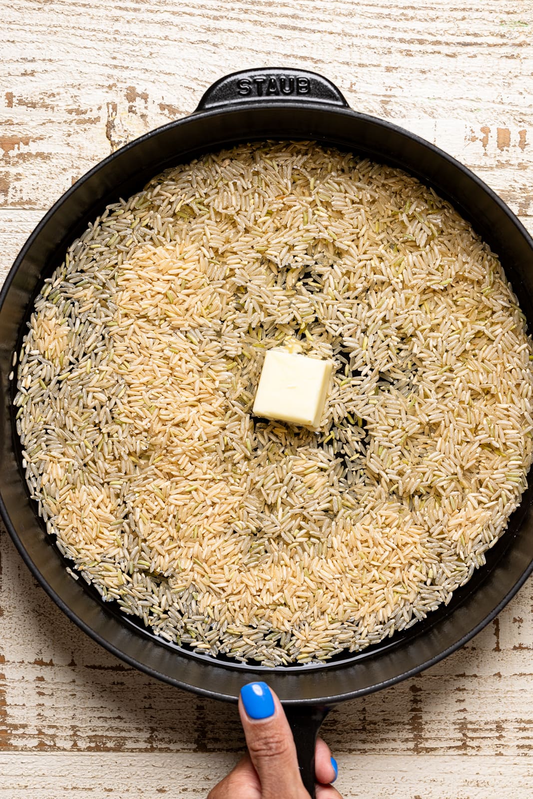 Rice in a black skillet with water and butter being held. 