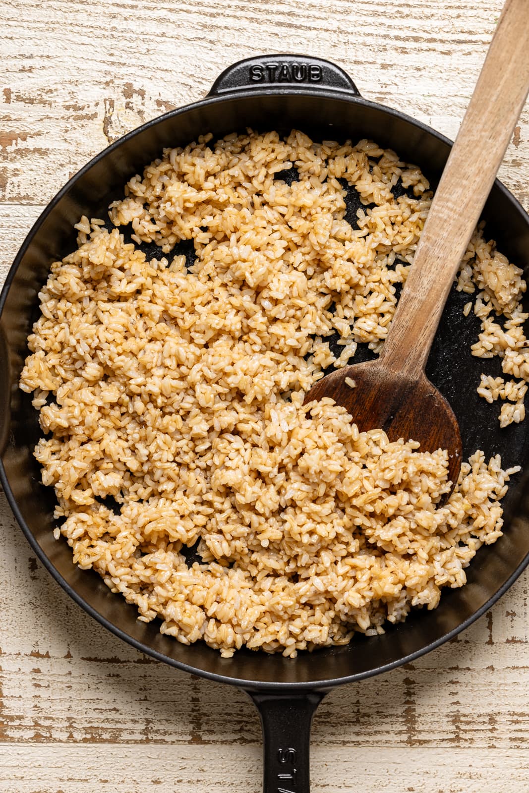 Cooked brown rice in a black skillet with wooden spoon. 