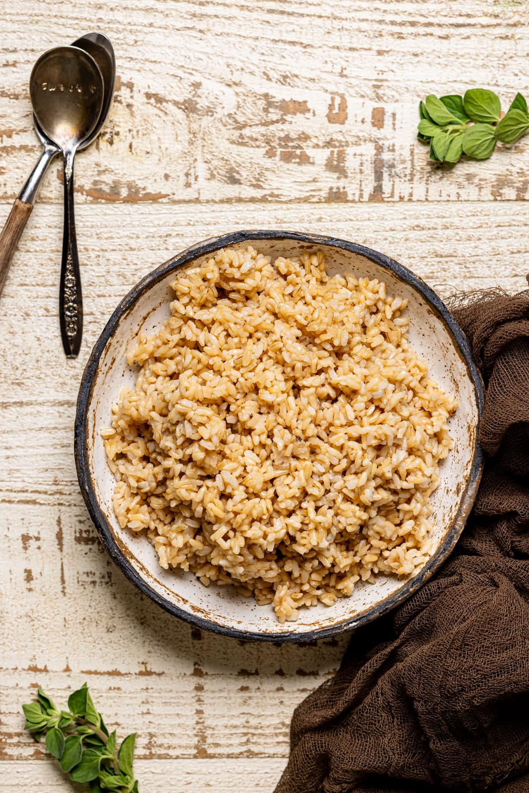 Cooked brown rice in a bowl with two spoons and a brown napkin.