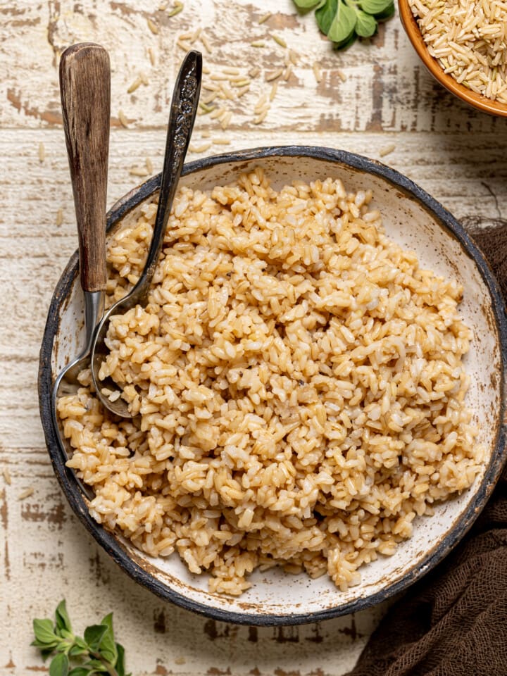 Rice in a bowl with spoons and herbs.