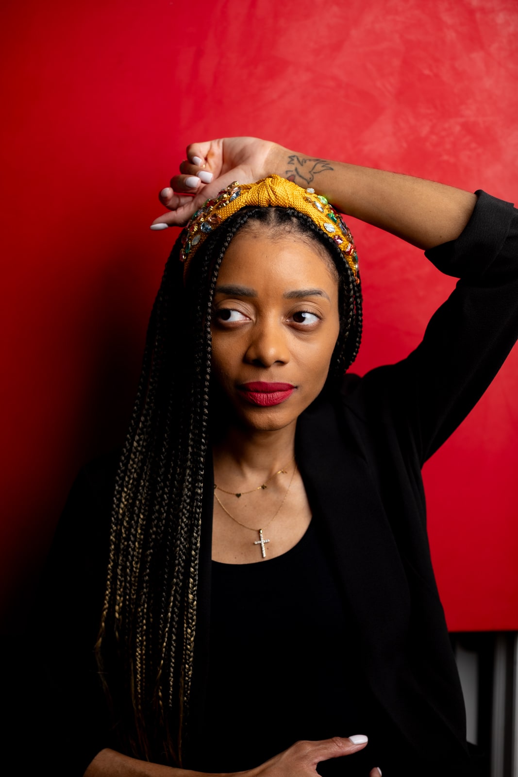 Shanika in a black shirt and blazer with a red background and one hand above her head.