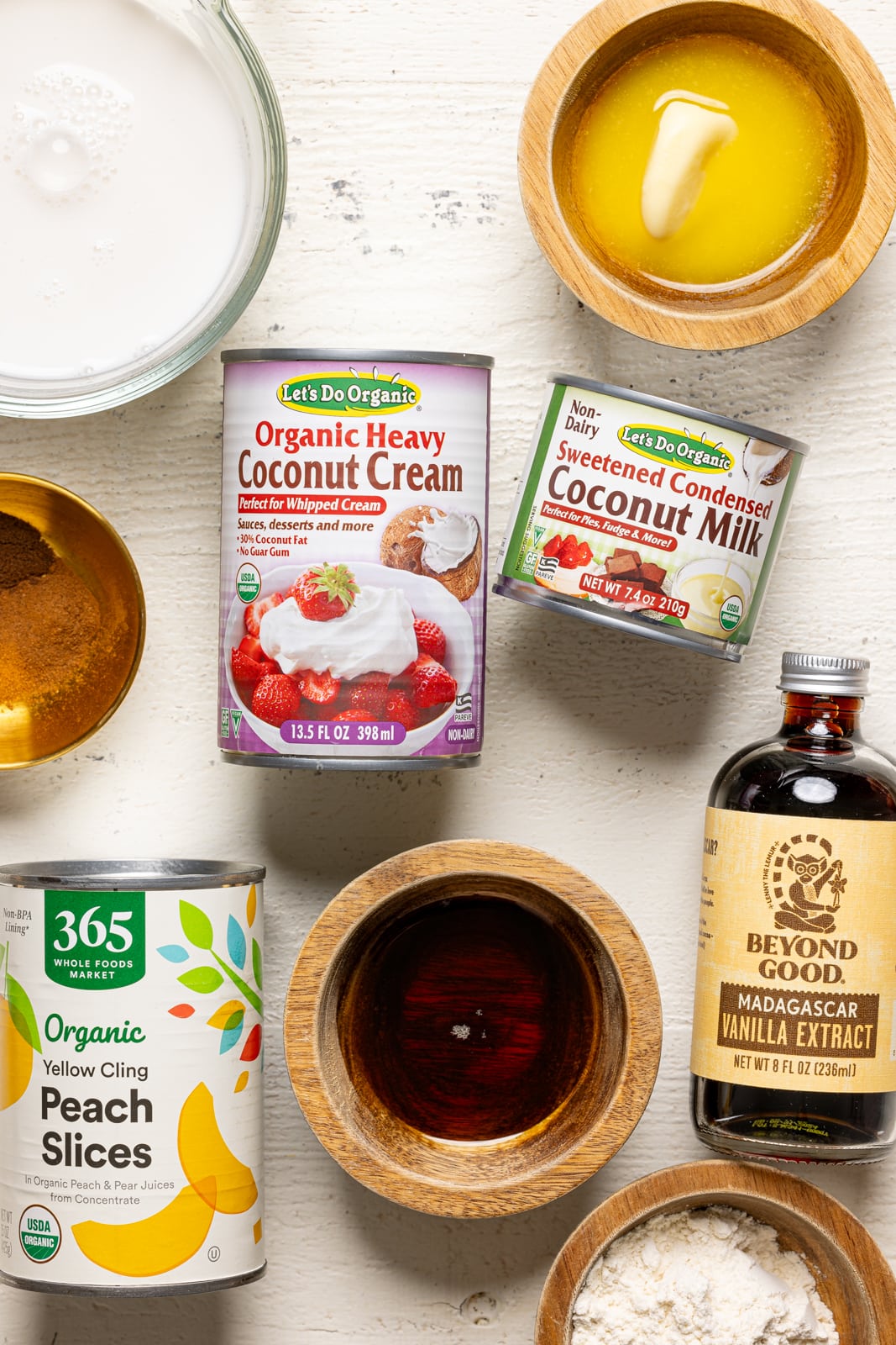 Ingredients on a white wood table including coconut cream, peaches, vanilla, milk, etc.