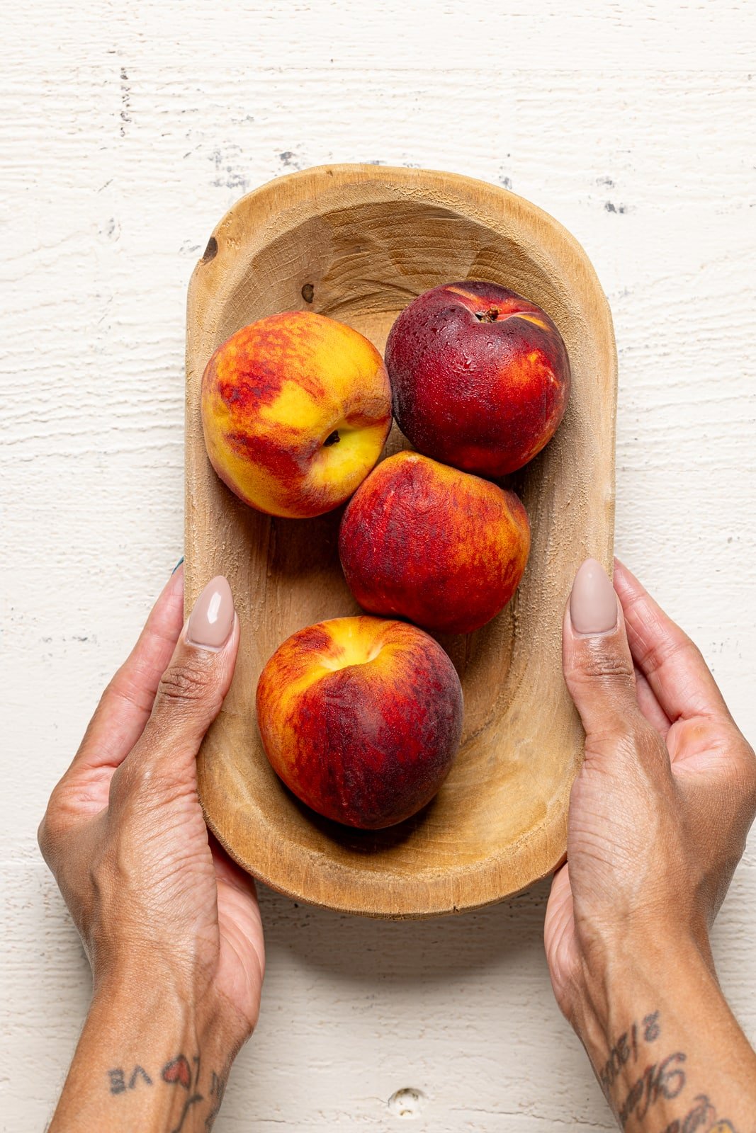Fresh peaches in a wood bowl being held.