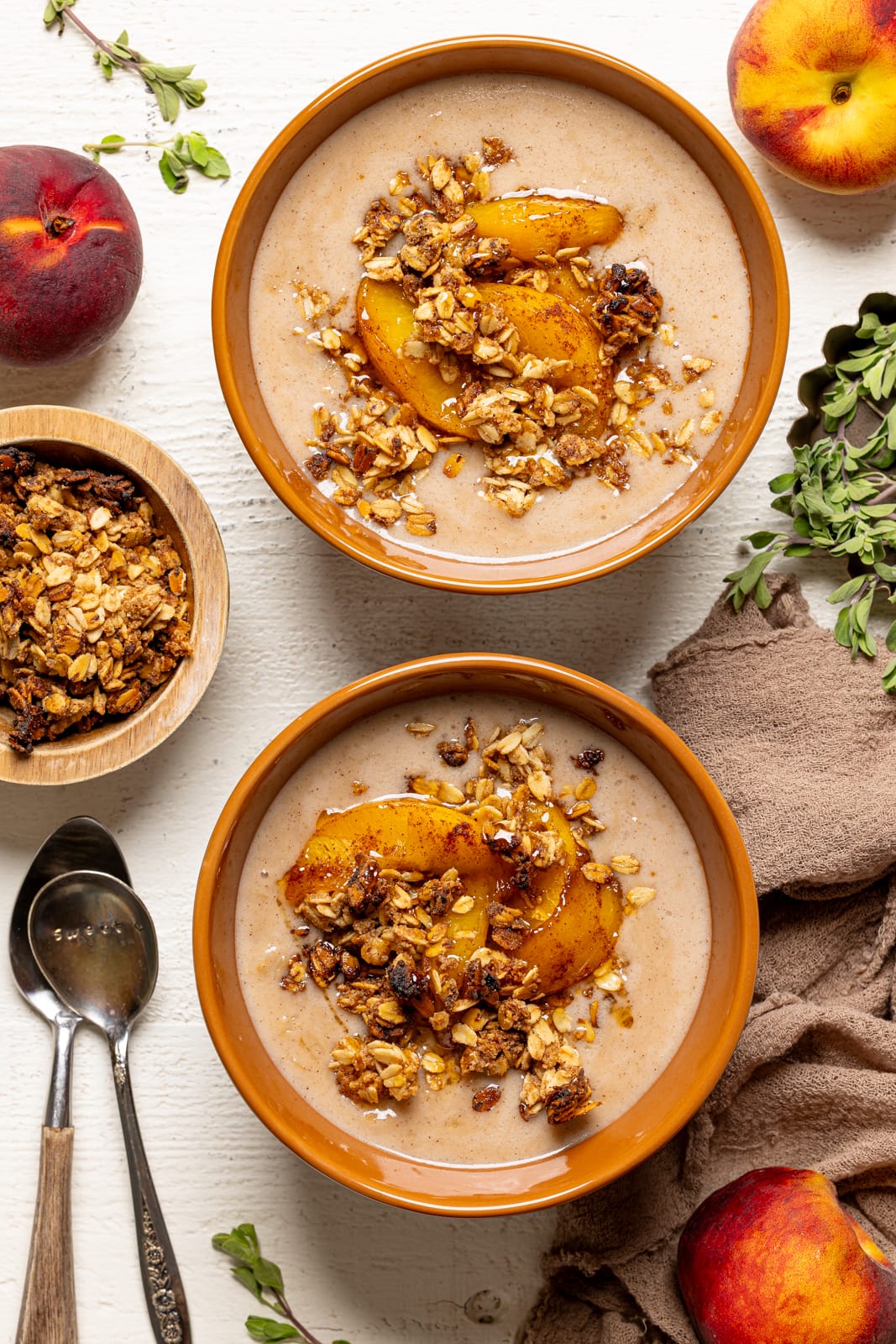Two bowls of porridge with peaches, granola, and two spoons. 