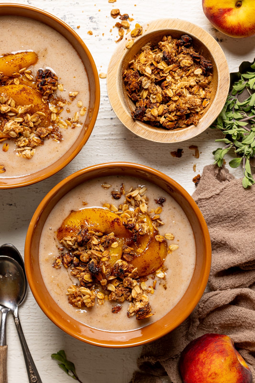 Bowl of oatmeal porridge with two spoons, peaches, and granola.