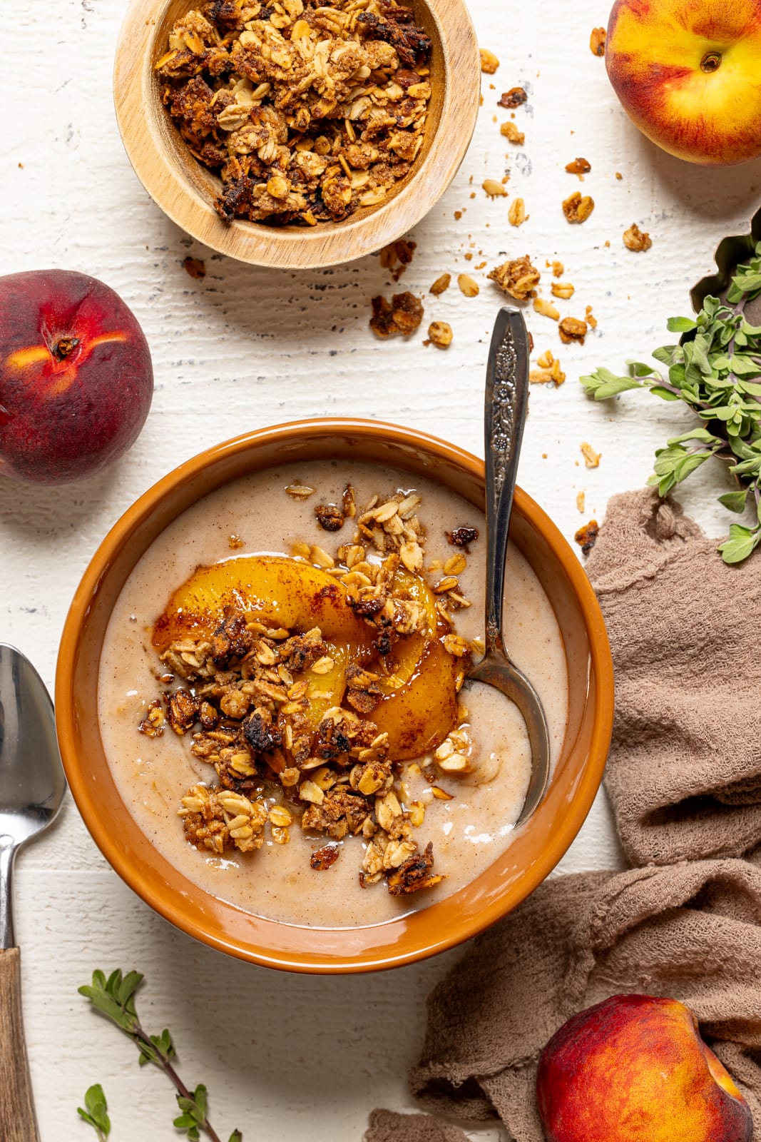 Bowl of porridge with a spoon, peaches, granola, and a side spoon.