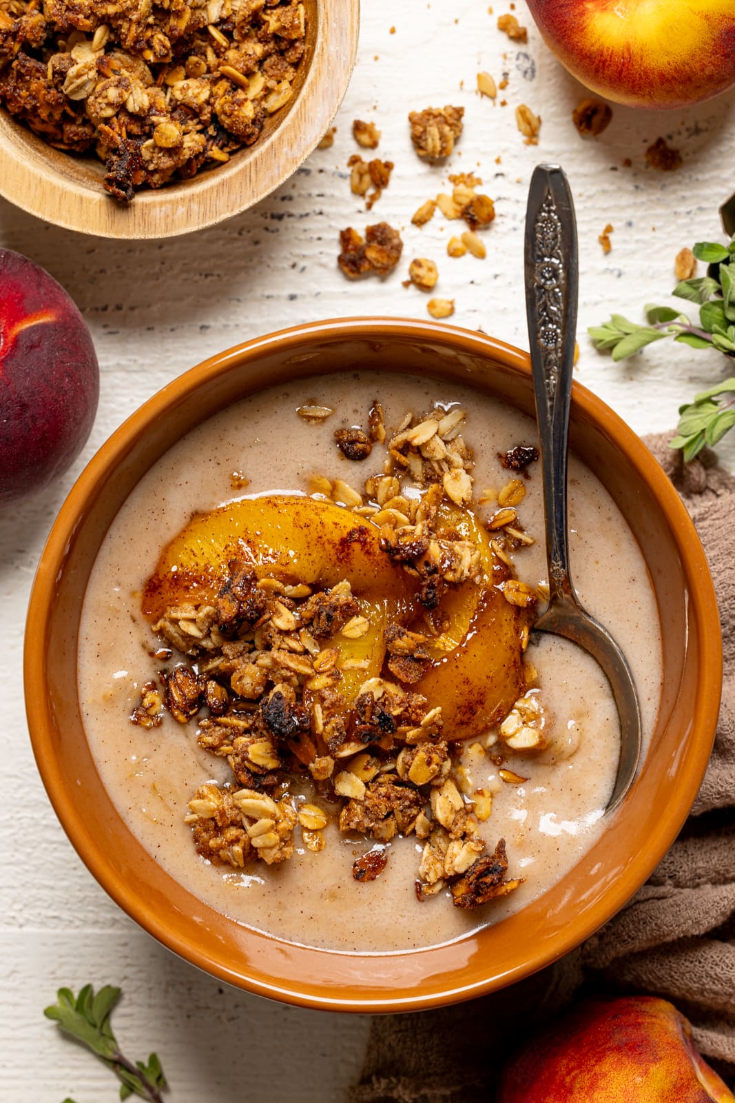 Up close shot of porridge in a bowl with a spoon, peaches, and granola. 