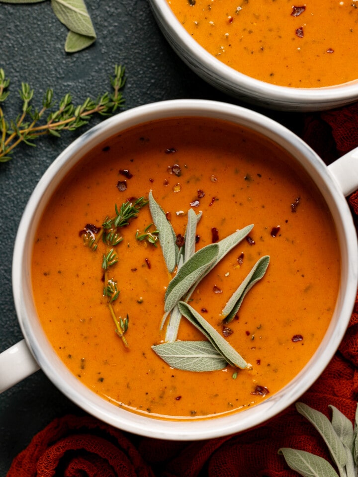 Soup in two white bowls with a garnish of sage and thyme.