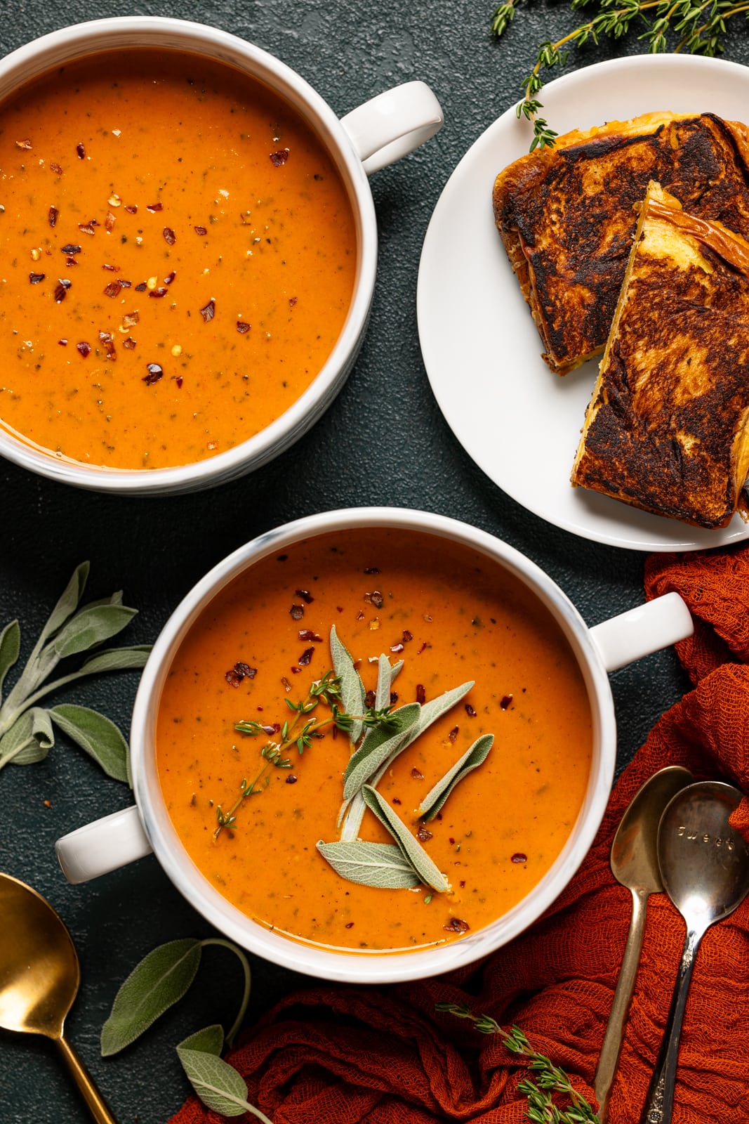Soups in two white bowls with grilled cheese and two spoons.