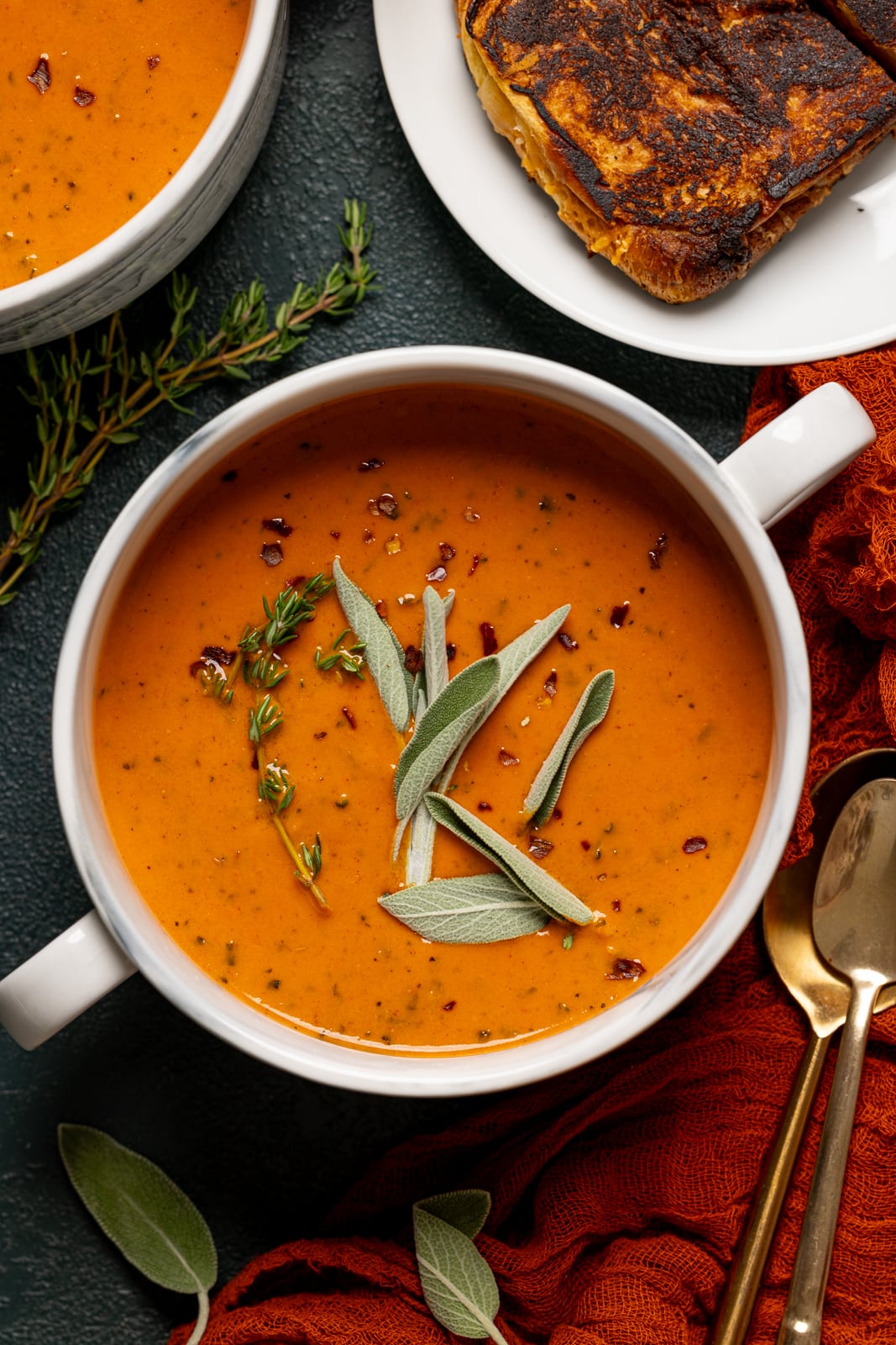 Up close shot of bowl of soup with grilled cheese and spoons.