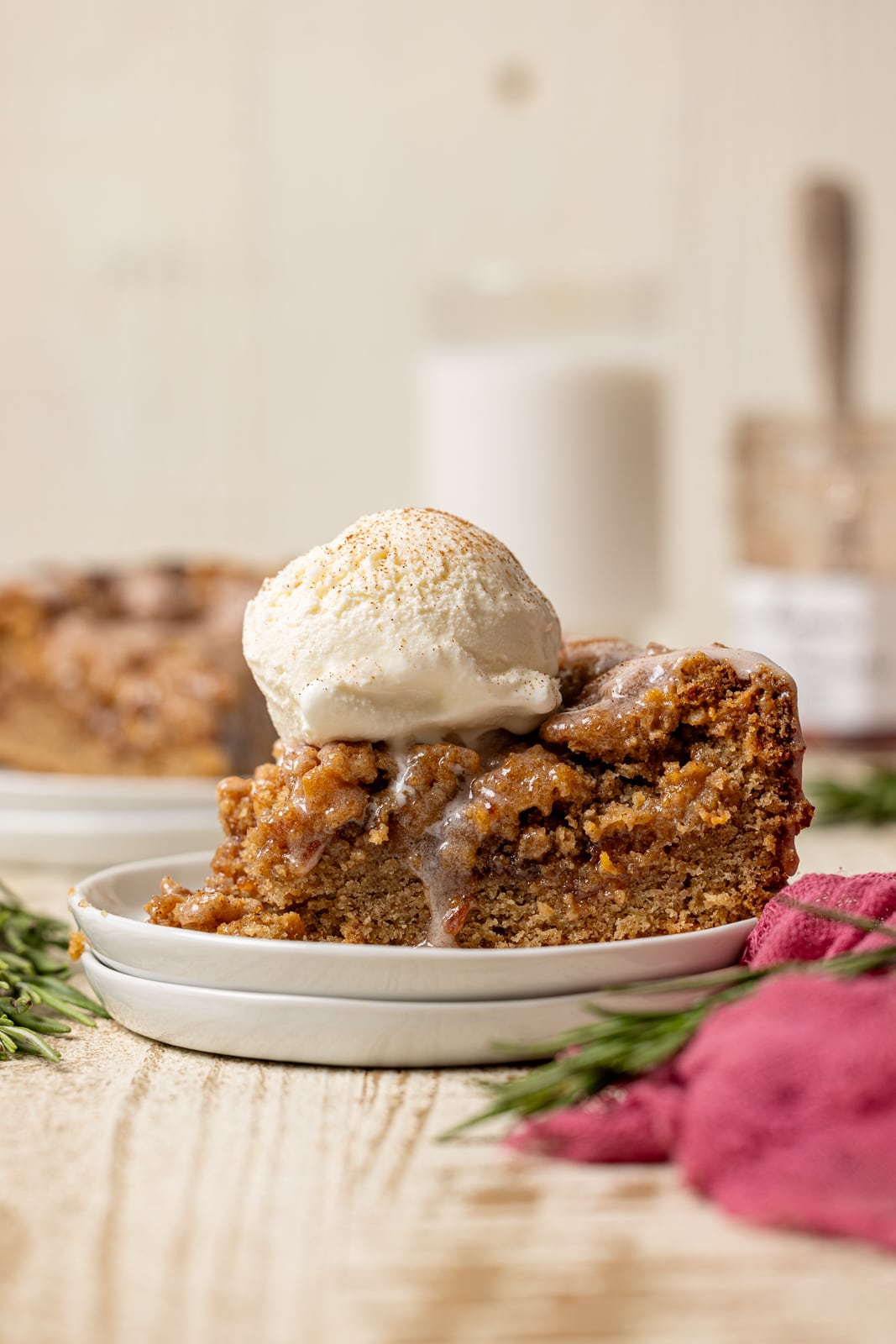 A slice strawberry crumb cake on a stack of plates with a scoop of ice cream and a glass of milk with jam in the background.