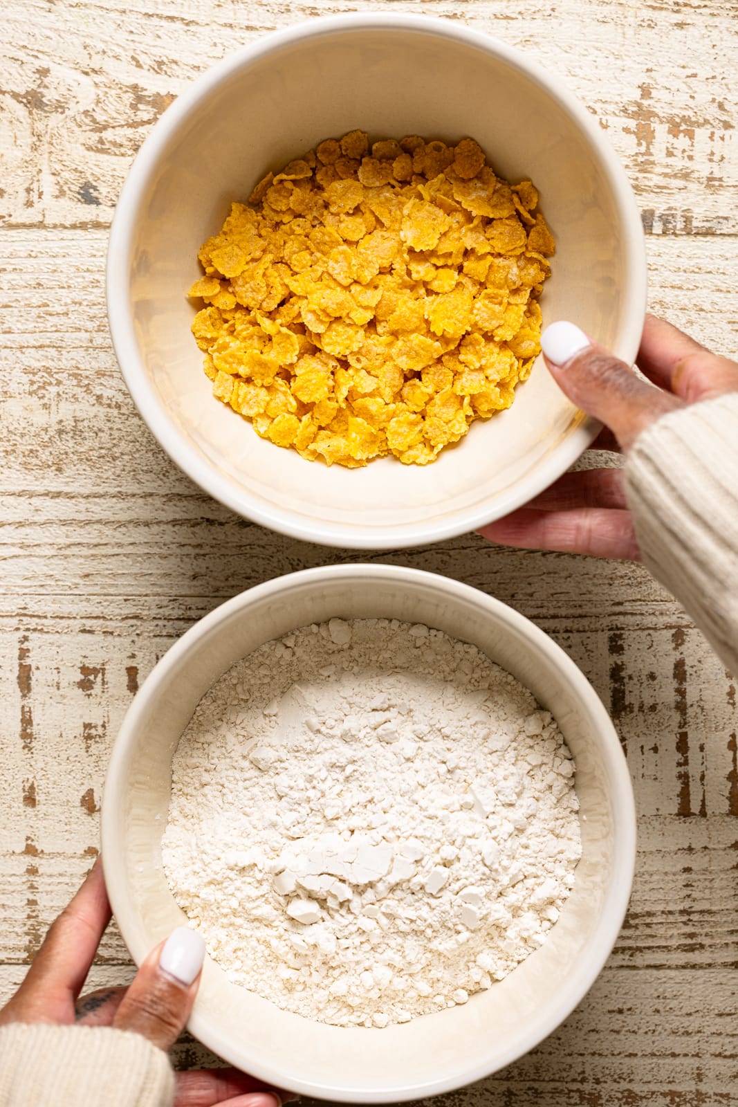 A bowl with flour and cornflakes being held. 