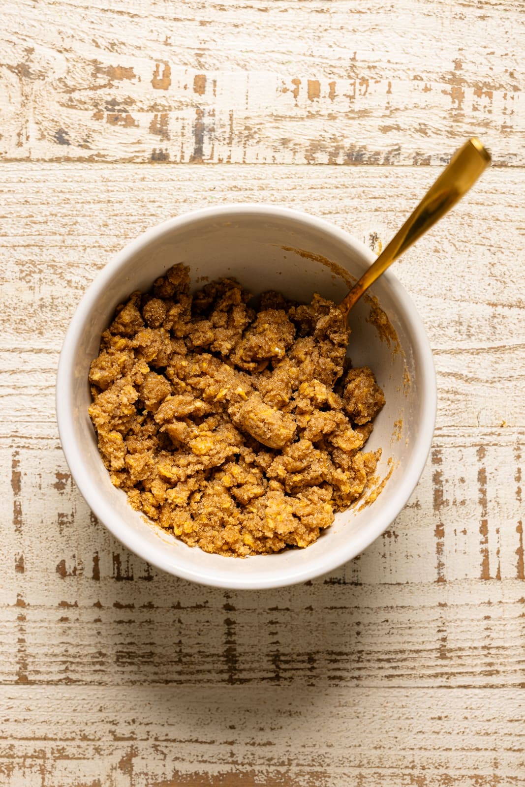 A bowl with crumble topping in a bowl with a gold spoon.