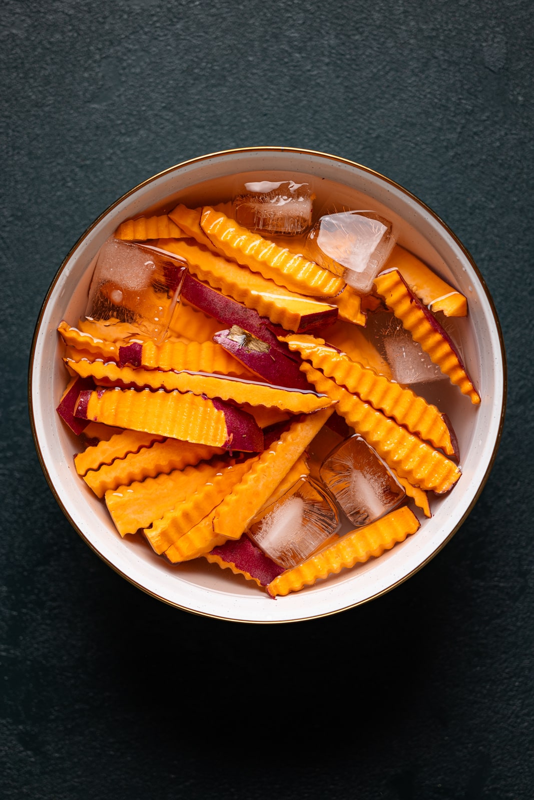 Sweet potatoes cut into fries in a bowl with water and ice.