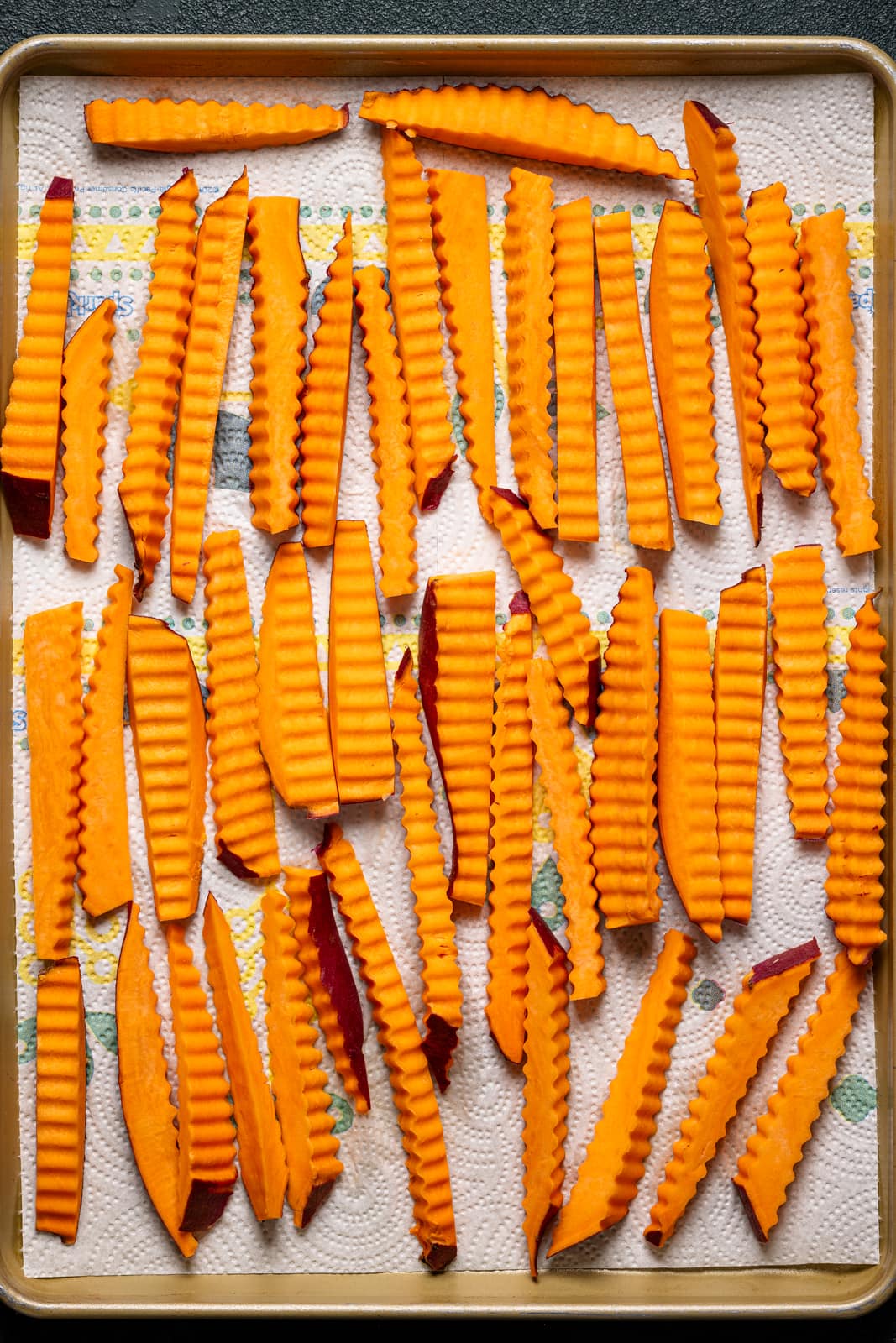 Sweet potato fries lined on a baking sheet with paper towel.