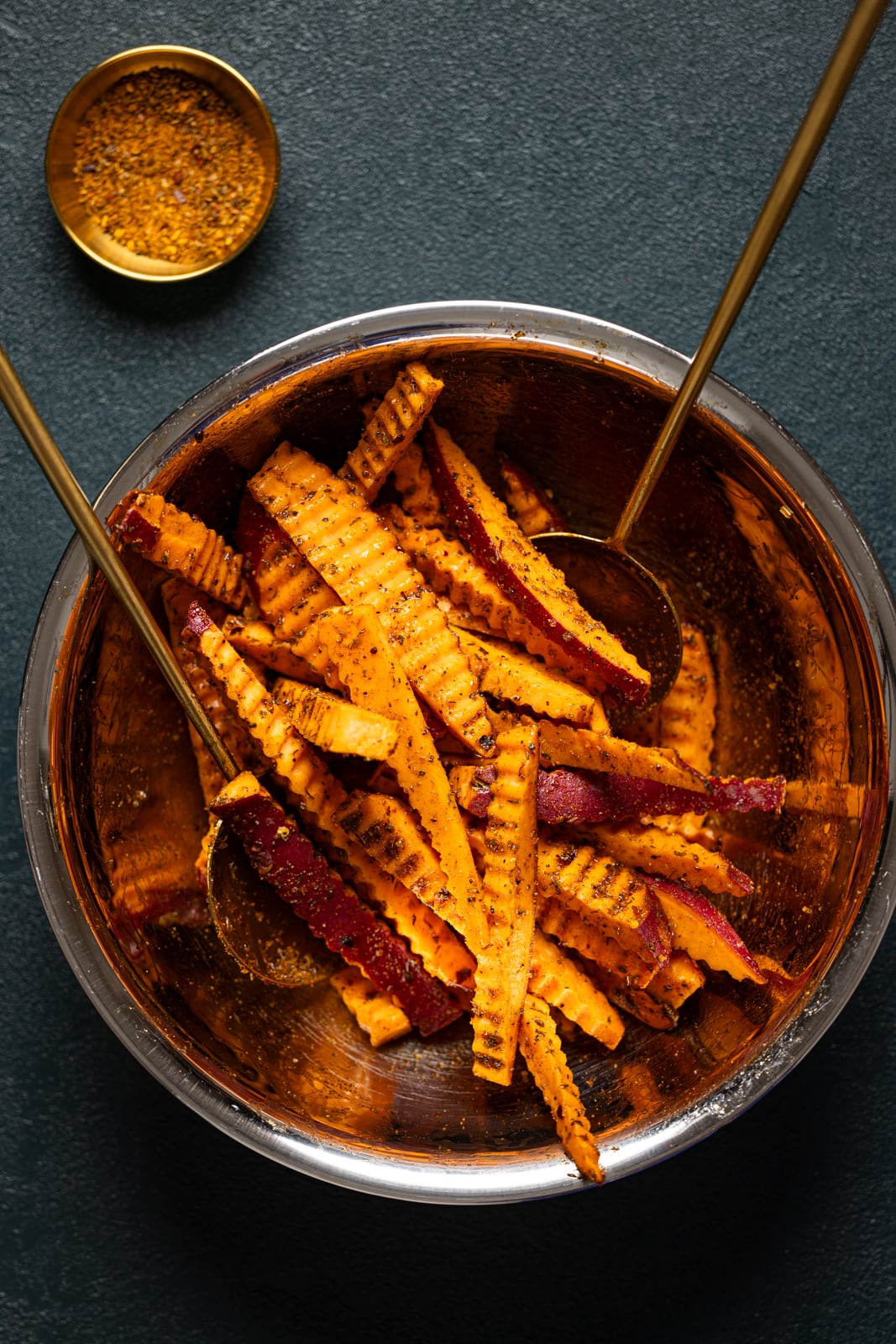 Fries in a bowl with cajun seasoning and two gold spoons.